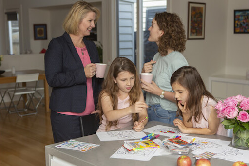 an aupair talking with the working mother while her children are engaged in art and craft